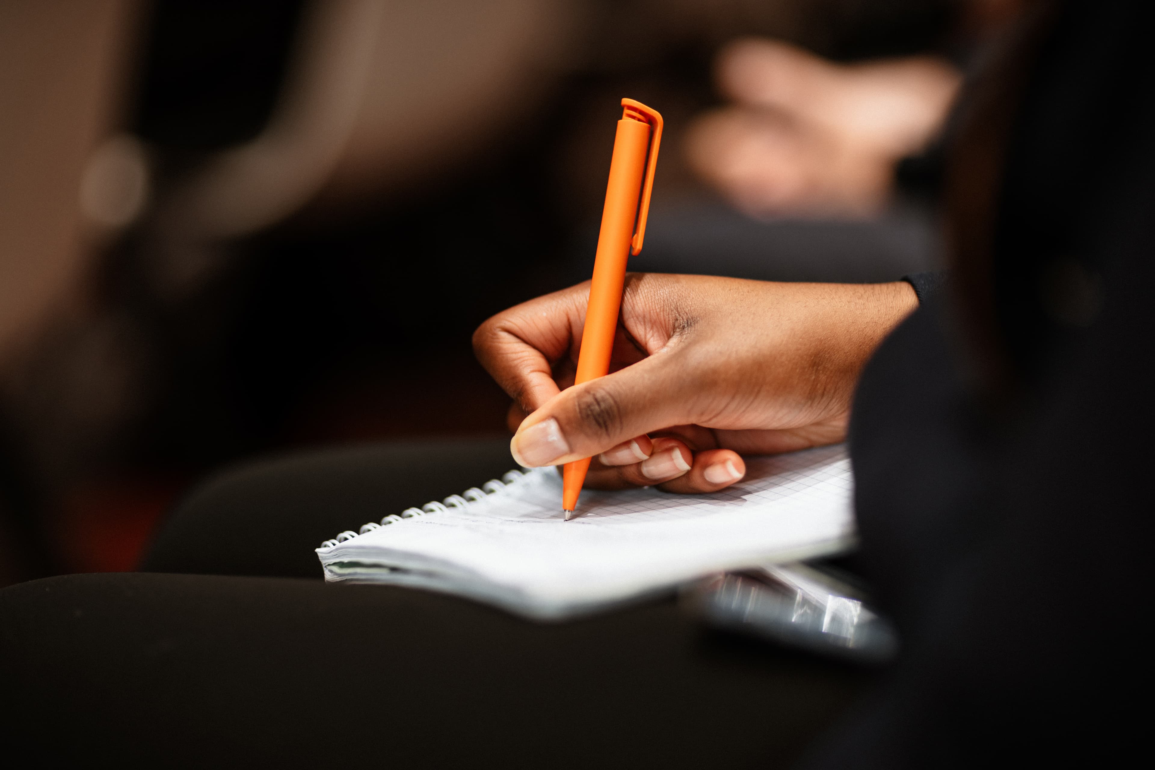Hand writing with an orange pen representing essay development